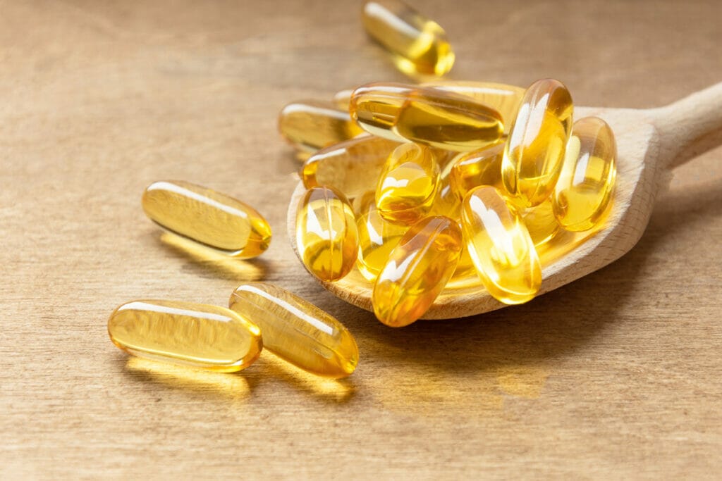 Cod liver oil omega 3 gel capsules on a spoon on wooden background. Fish oil vitamins.